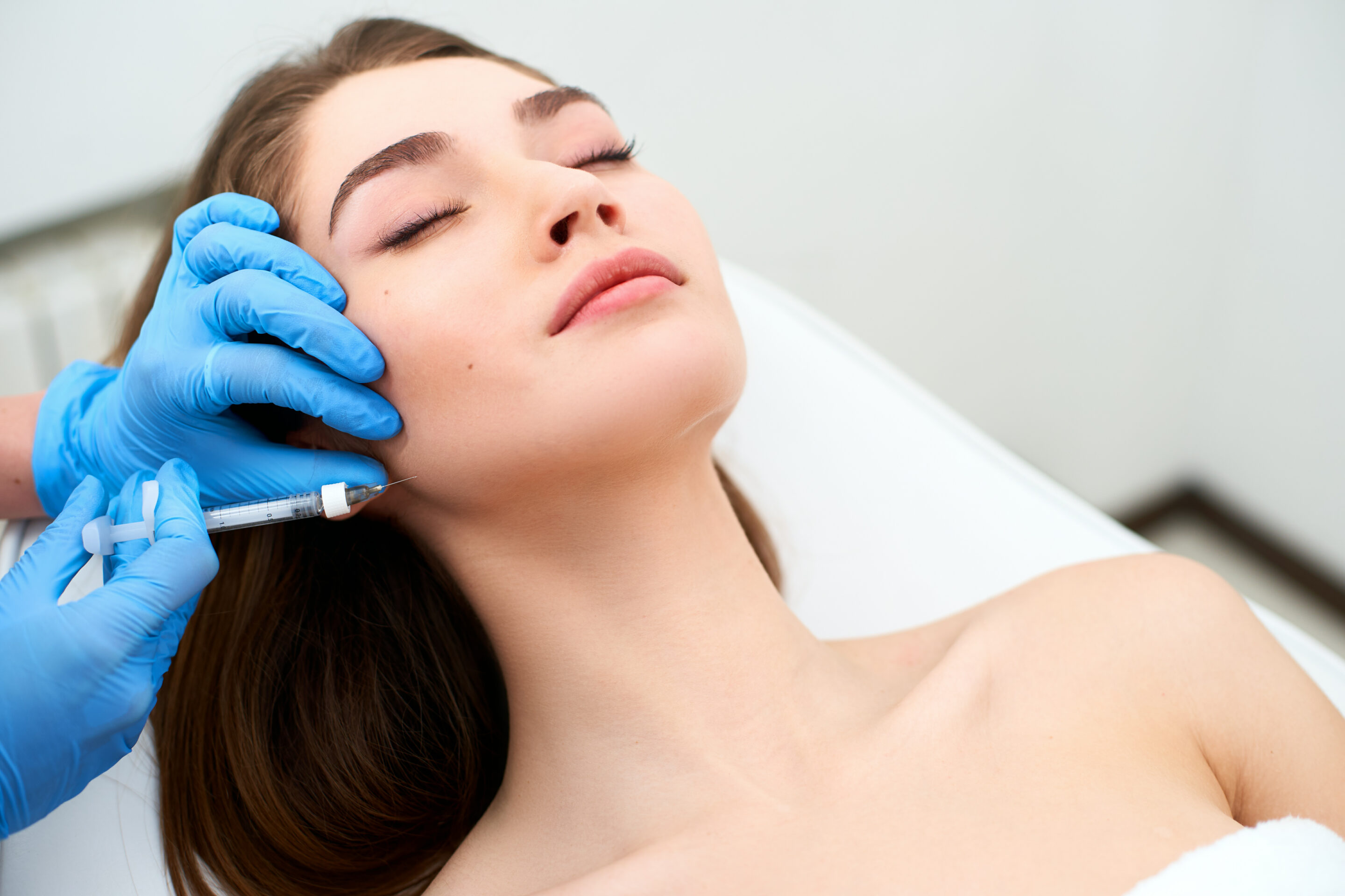 Beautician doctor with filler syringe making injection to jowls. Masseter lines reduction and face contouring therapy. Anti aging treatment and face lift in cosmetology clinic. Patient lying on chair injctable fillers
